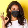 Concept of coronavirus, pandemic and lifestyle. Close-up of cheeky african-american girl in black face mask, showing okay sign and winking, recommending something, yellow background.
